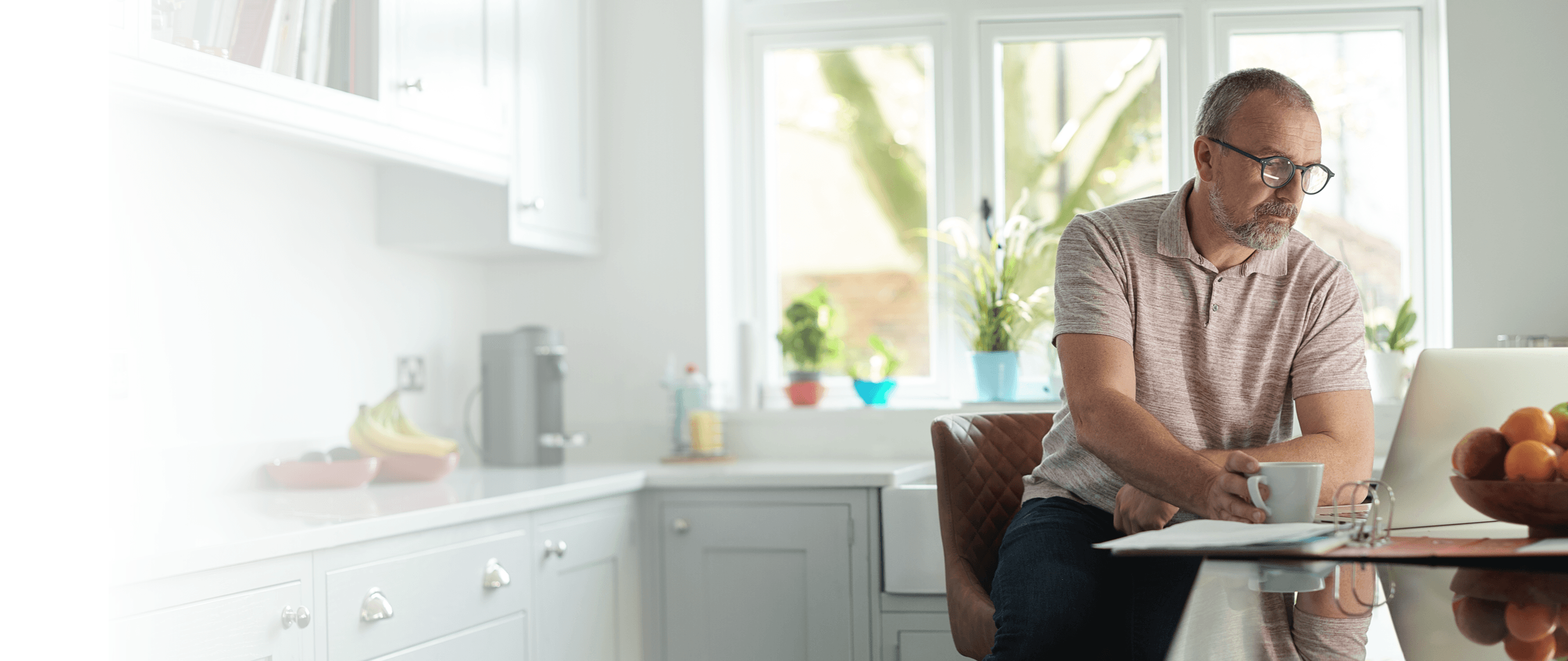 A man sits at a table using a computer in a kitchen.